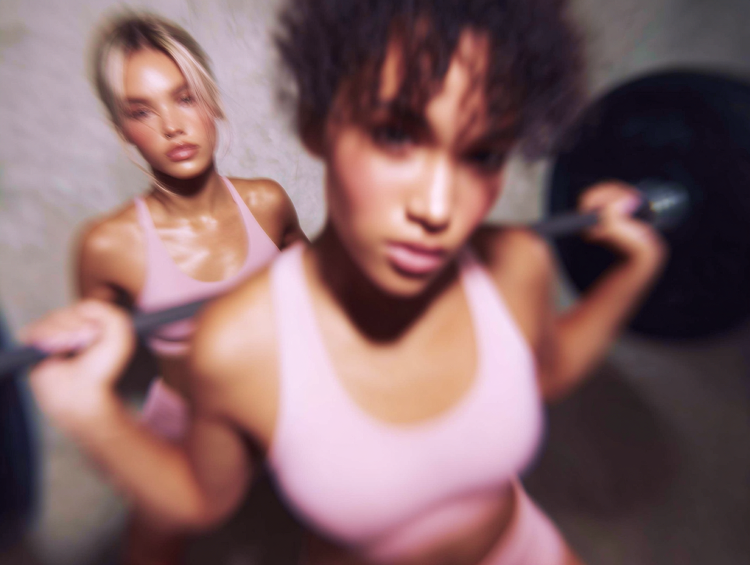 Zwei Frauen in rosa Sportbekleidung sind in einem Fitnessstudio am trainieren. Die vordere Frau hat eine Langhantel auf dem Rücken und macht Kniebeugen, die hintere leistet Hilfestellung.