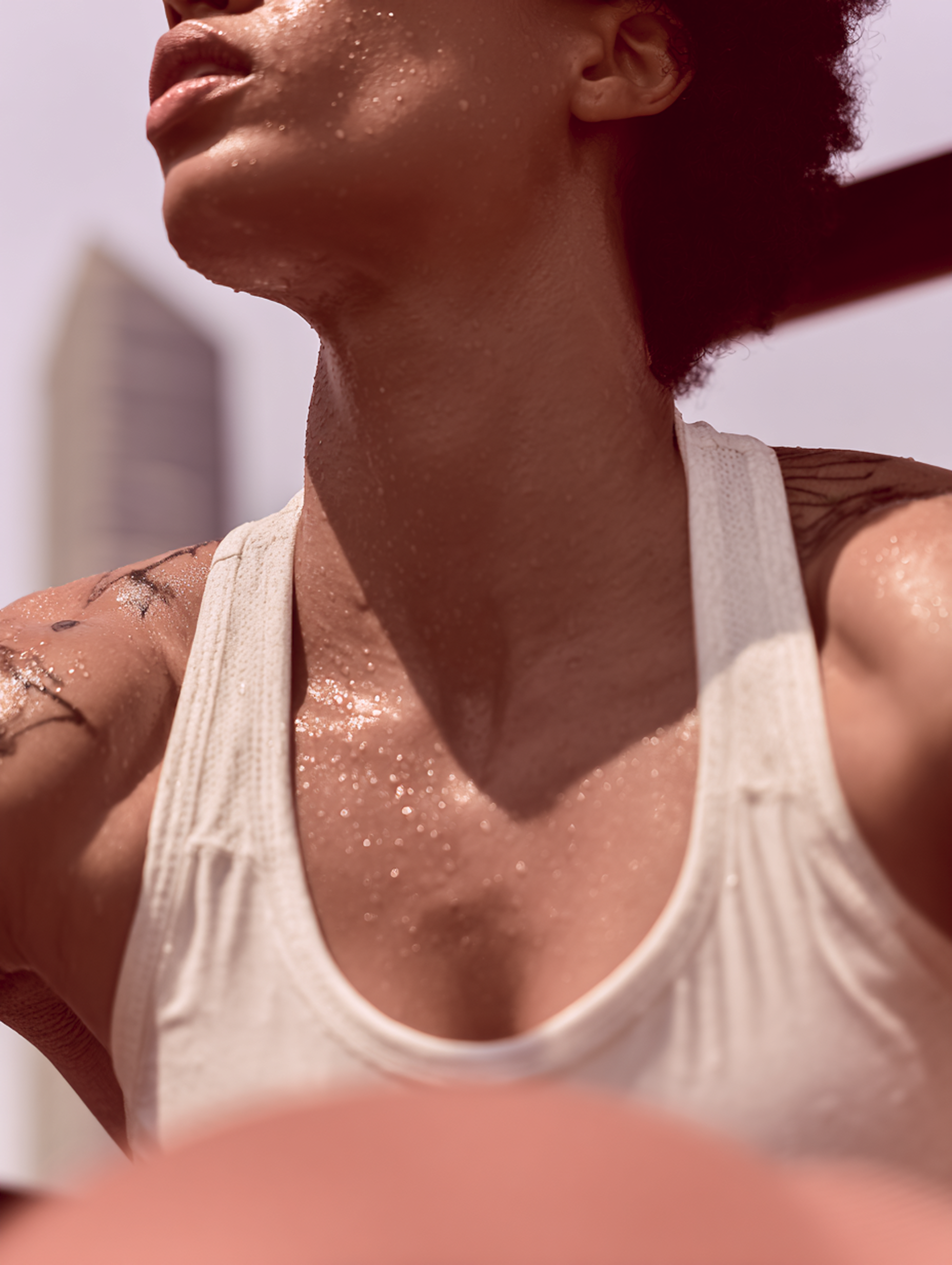 Nahaufnahme einer konzentrierten Frau mit athletischem Körperbau, die vor Schweiß glänzt und ein beigen Tanktop trägt.