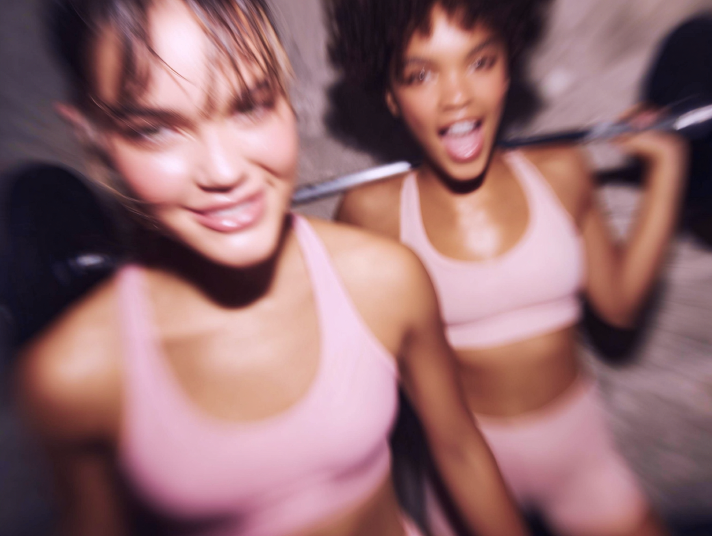 Zwei Frauen in pinkfarbener Sportbekleidung heben eine Hantel und konzentrieren sich auf ihr Training in einem Fitnessstudio.